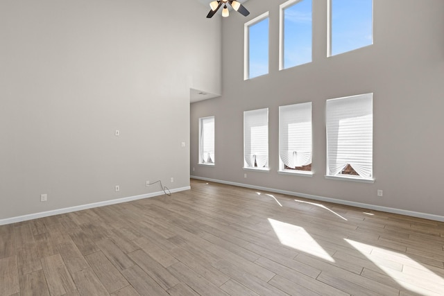 unfurnished living room with ceiling fan, light wood finished floors, and baseboards