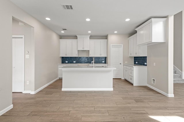 kitchen featuring light wood finished floors, baseboards, visible vents, an island with sink, and a sink