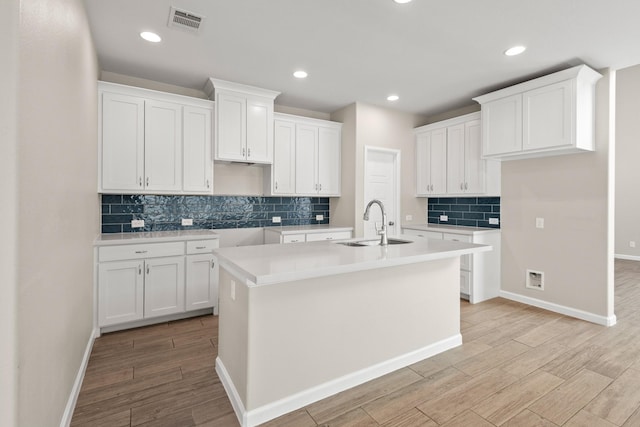 kitchen with white cabinets, a sink, light wood-style flooring, and a center island with sink