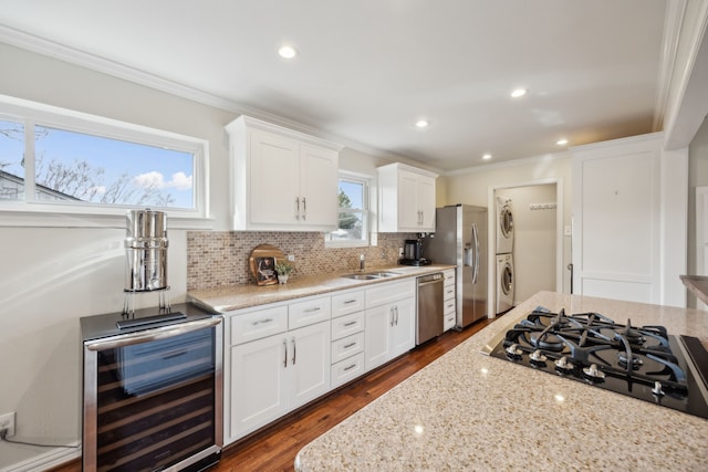 kitchen with stacked washer and dryer, stainless steel appliances, backsplash, a sink, and beverage cooler