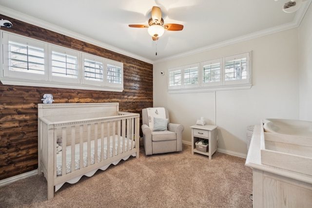 bedroom featuring carpet floors, ornamental molding, ceiling fan, a crib, and baseboards