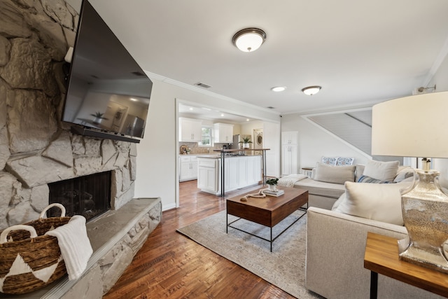 living area with a fireplace, visible vents, crown molding, and wood finished floors