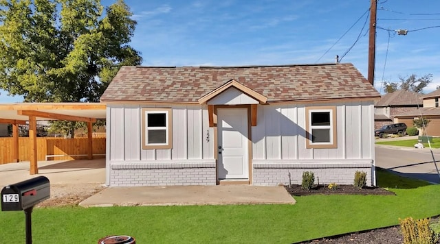 view of front of house featuring roof with shingles, fence, an outdoor structure, board and batten siding, and a front yard