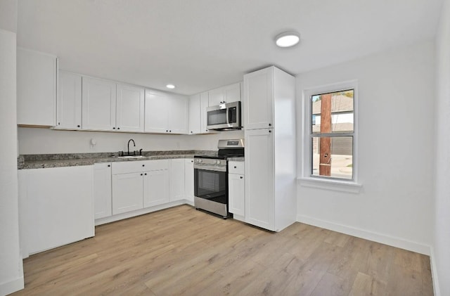 kitchen with stainless steel appliances, white cabinetry, a sink, and light wood-style flooring