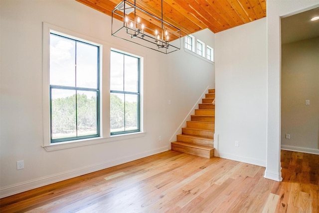 staircase with a notable chandelier, wood finished floors, wood ceiling, and baseboards