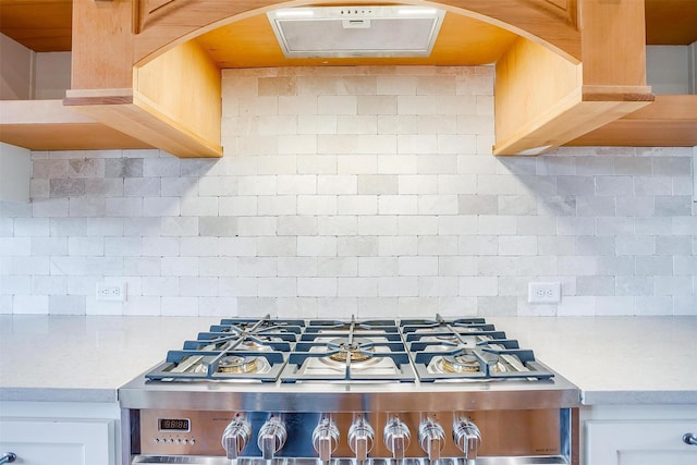 kitchen featuring light countertops, decorative backsplash, white cabinets, gas range, and exhaust hood