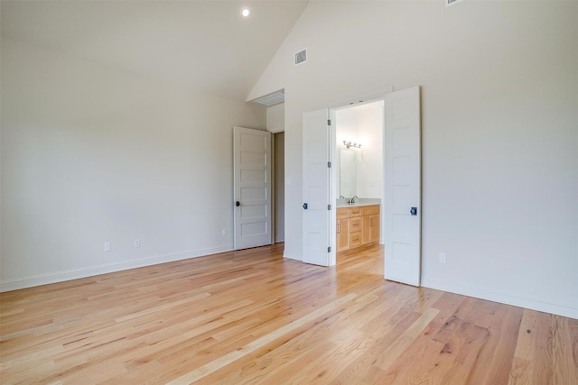 unfurnished bedroom featuring high vaulted ceiling, a sink, visible vents, baseboards, and light wood finished floors