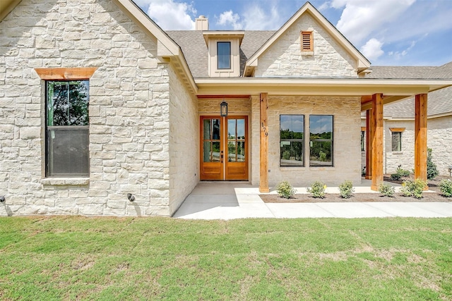 view of exterior entry featuring stone siding, french doors, a yard, and a shingled roof