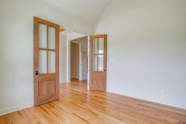 spare room with vaulted ceiling, baseboards, and light wood-style floors