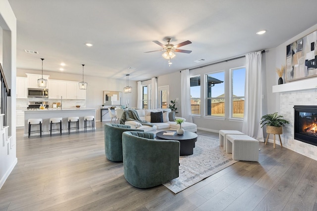 living area featuring recessed lighting, a fireplace, visible vents, baseboards, and light wood finished floors