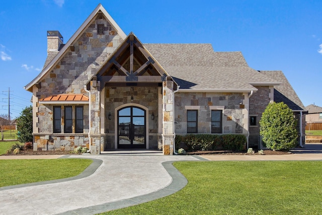 view of front of property featuring a shingled roof, stone siding, a chimney, french doors, and a front lawn