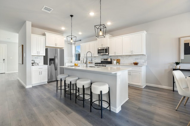 kitchen with a center island with sink, a breakfast bar area, stainless steel appliances, visible vents, and dark wood-type flooring