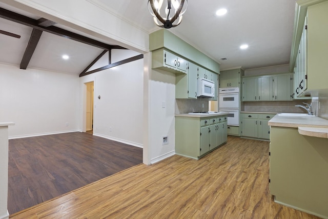 kitchen with white appliances, a sink, green cabinets, light countertops, and backsplash