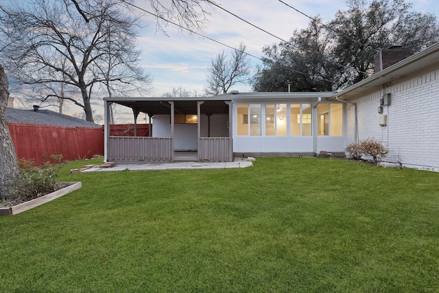 back of house with a sunroom, brick siding, a lawn, and fence