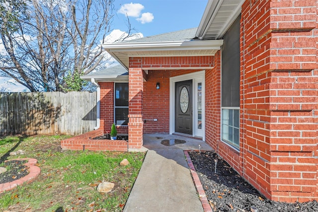 property entrance with brick siding, fence, and roof with shingles