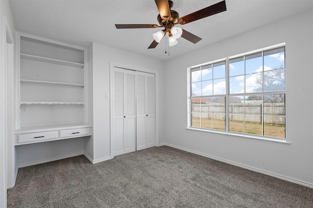 unfurnished bedroom featuring baseboards, built in study area, a textured ceiling, and carpet flooring