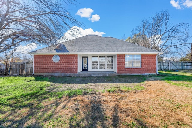 back of property with a shingled roof, brick siding, a lawn, and fence