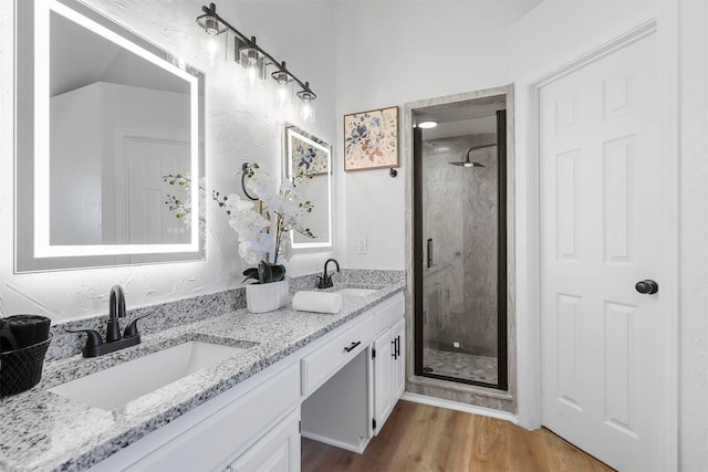 full bathroom with double vanity, wood finished floors, a stall shower, and a sink