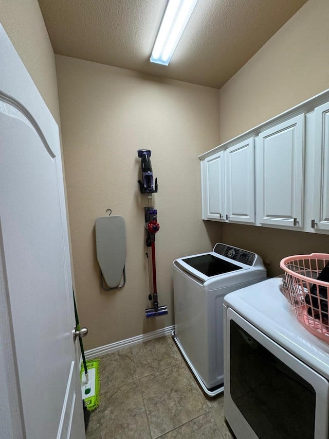 washroom with cabinet space, light tile patterned floors, baseboards, washer and clothes dryer, and a textured ceiling