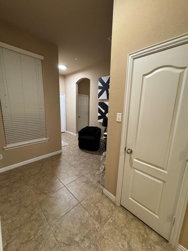 hall with light tile patterned floors, baseboards, and arched walkways