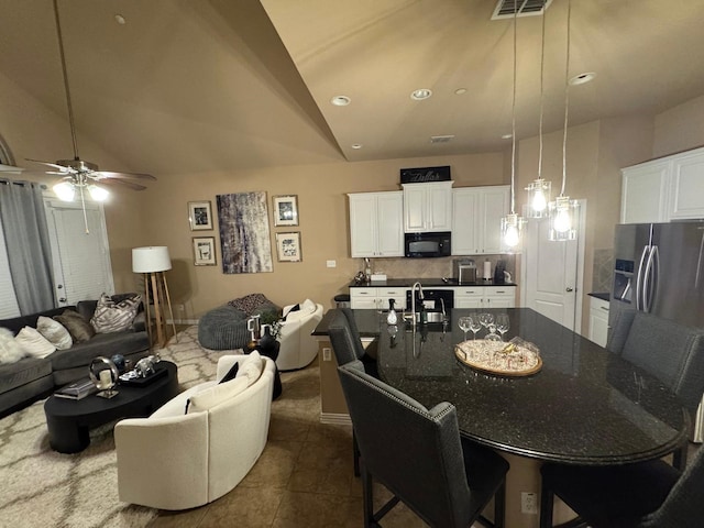 interior space with a ceiling fan, dark tile patterned flooring, visible vents, and vaulted ceiling