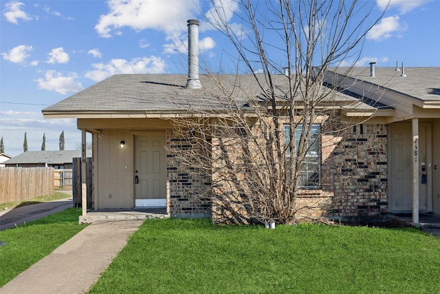 view of exterior entry with brick siding, a lawn, and fence