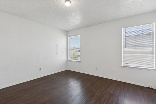 empty room featuring a textured ceiling, dark wood-type flooring, plenty of natural light, and baseboards