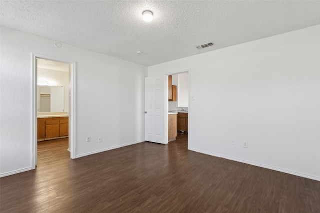 unfurnished bedroom featuring a textured ceiling, dark wood-type flooring, visible vents, and baseboards