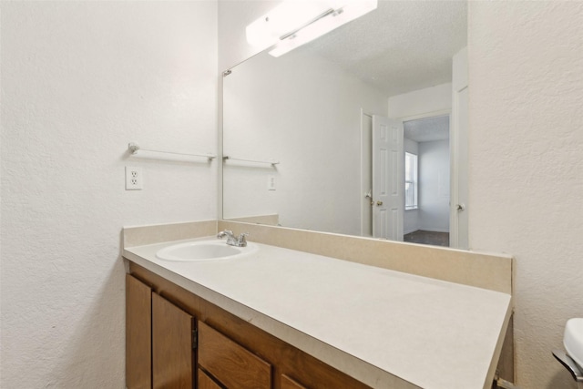 bathroom with toilet, a textured wall, a textured ceiling, and vanity