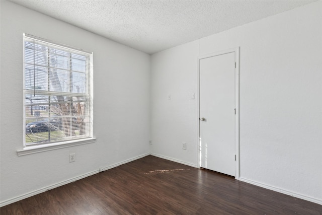 spare room with a textured ceiling, wood finished floors, a wealth of natural light, and baseboards