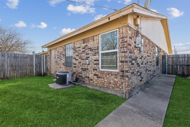 view of side of property with brick siding, a lawn, a fenced backyard, and central air condition unit