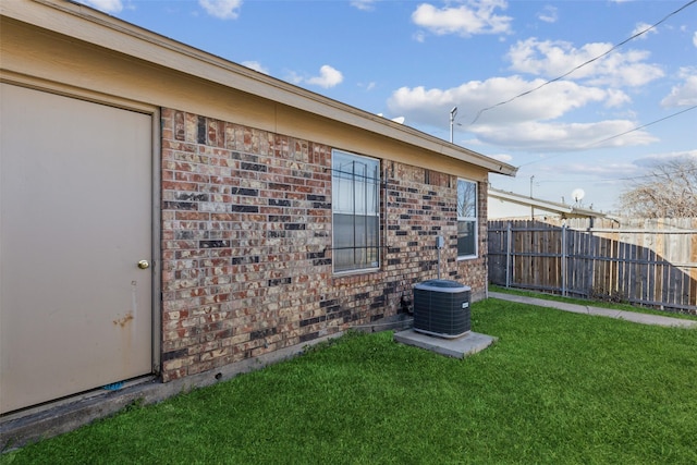 view of home's exterior with brick siding, a lawn, cooling unit, and fence