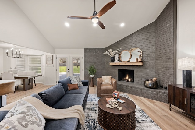 living area featuring french doors, a brick fireplace, wood finished floors, high vaulted ceiling, and ceiling fan with notable chandelier