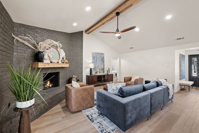 living area featuring beam ceiling, a fireplace, visible vents, brick wall, and light wood-type flooring