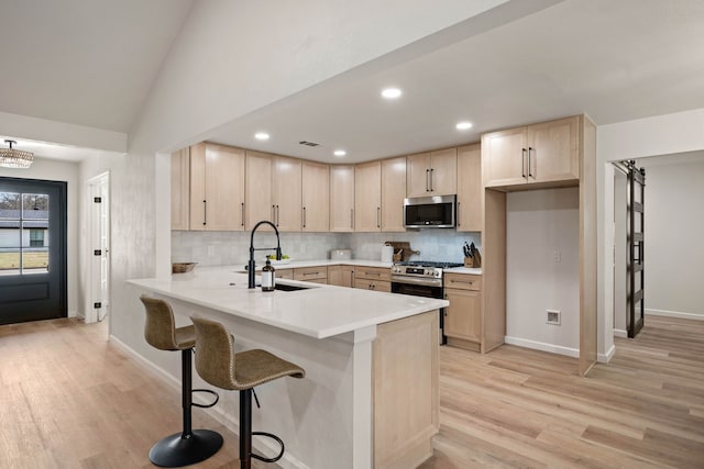 kitchen with a peninsula, stainless steel appliances, a sink, and light brown cabinetry