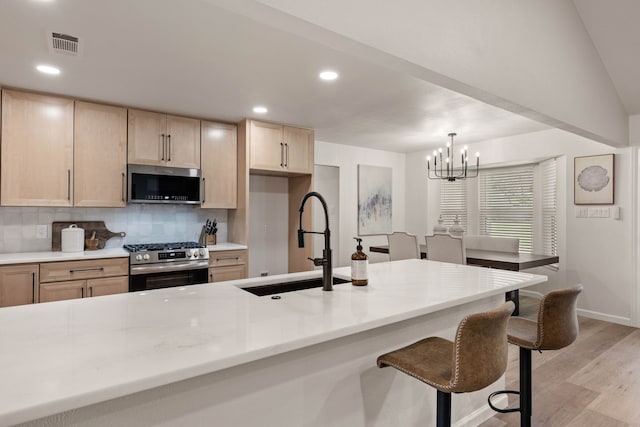 kitchen with light brown cabinets, stainless steel appliances, a sink, light wood-type flooring, and tasteful backsplash