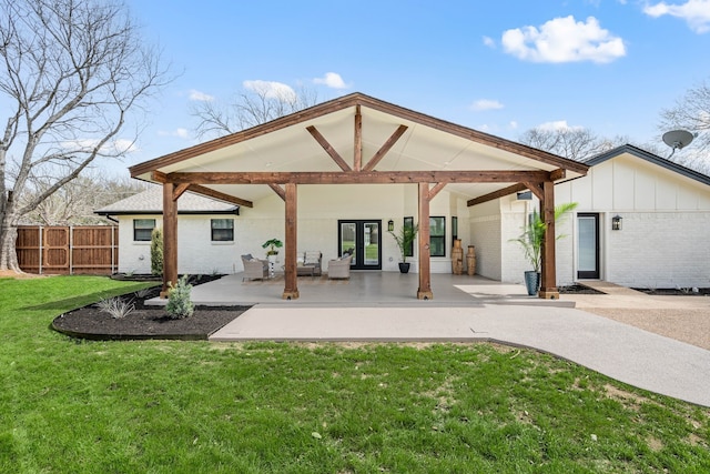 back of house with brick siding, a lawn, board and batten siding, a patio area, and fence