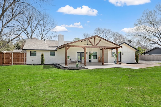 rear view of property featuring a patio, brick siding, fence, a yard, and a chimney