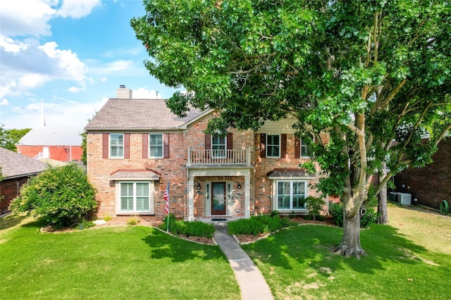 view of front of house with brick siding, a chimney, a front yard, and a balcony