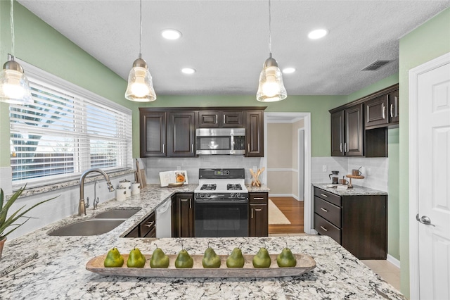 kitchen with a sink, visible vents, dark brown cabinets, stainless steel microwave, and gas stove