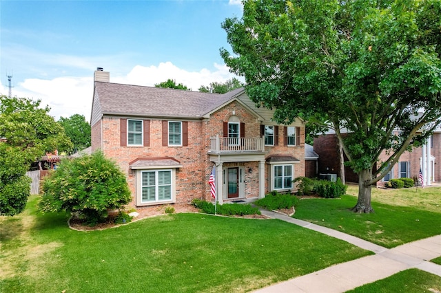 view of front facade with a balcony, a chimney, a front lawn, and brick siding