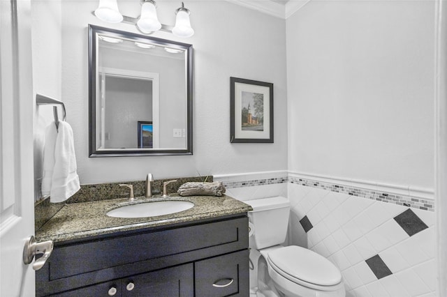 half bath with toilet, vanity, tile walls, ornamental molding, and wainscoting