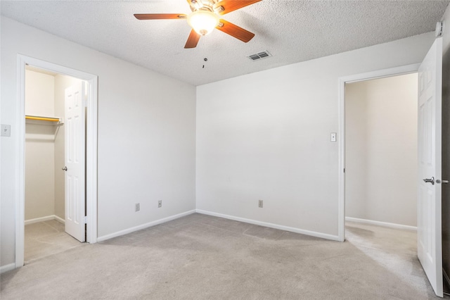 unfurnished bedroom featuring visible vents, a walk in closet, a textured ceiling, and light colored carpet