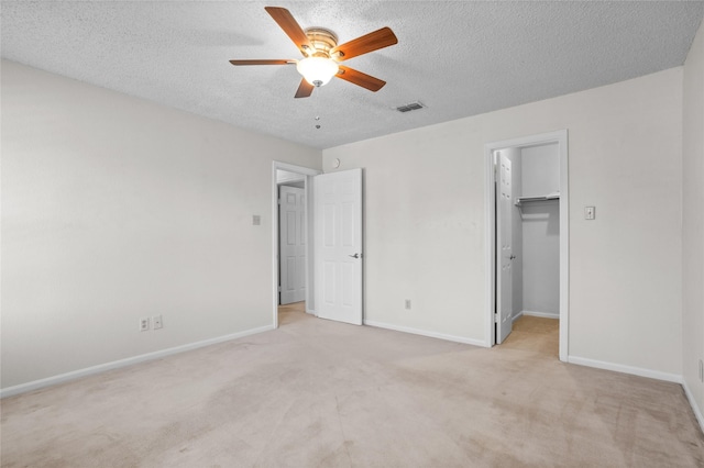 unfurnished bedroom featuring visible vents, a spacious closet, light carpet, a textured ceiling, and baseboards