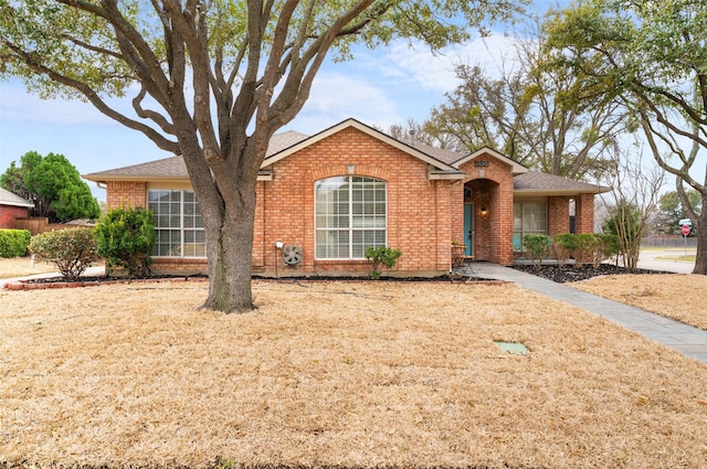 ranch-style home with a shingled roof, brick siding, and a front lawn