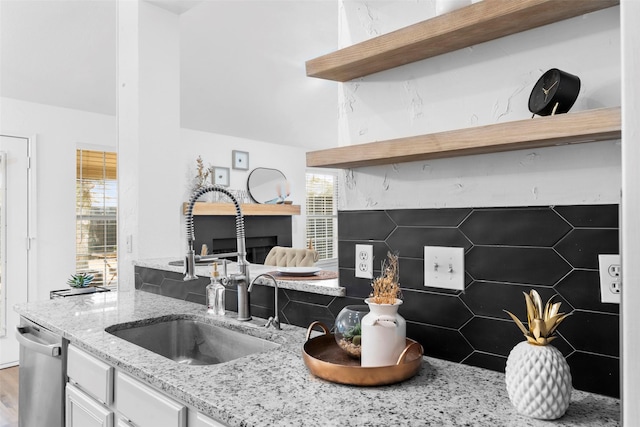 kitchen with open shelves, white cabinets, a sink, light stone countertops, and dishwasher