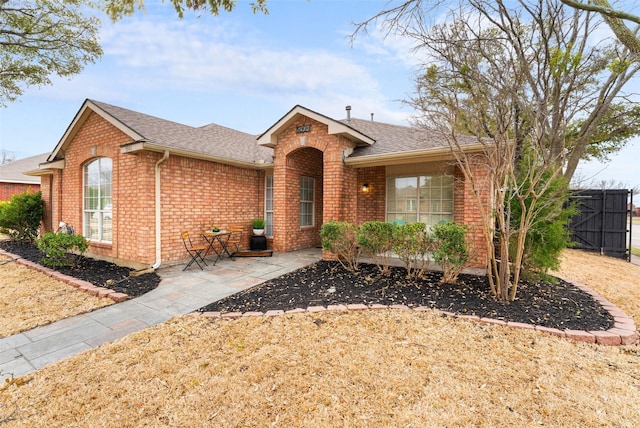 ranch-style home featuring a shingled roof, a gate, fence, and brick siding