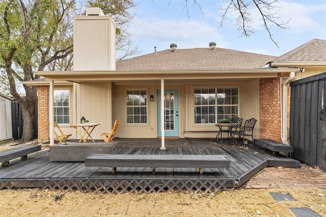 back of property featuring roof with shingles, brick siding, a chimney, and a wooden deck