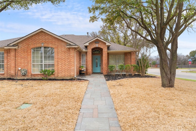 ranch-style home featuring brick siding and roof with shingles