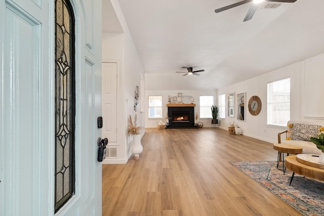 entryway featuring light wood-style floors, a warm lit fireplace, baseboards, and a ceiling fan